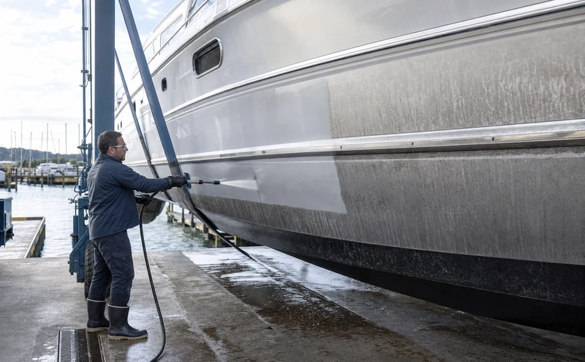 Boatyard worker cleaning a yacht hull while the vessel is in a lift