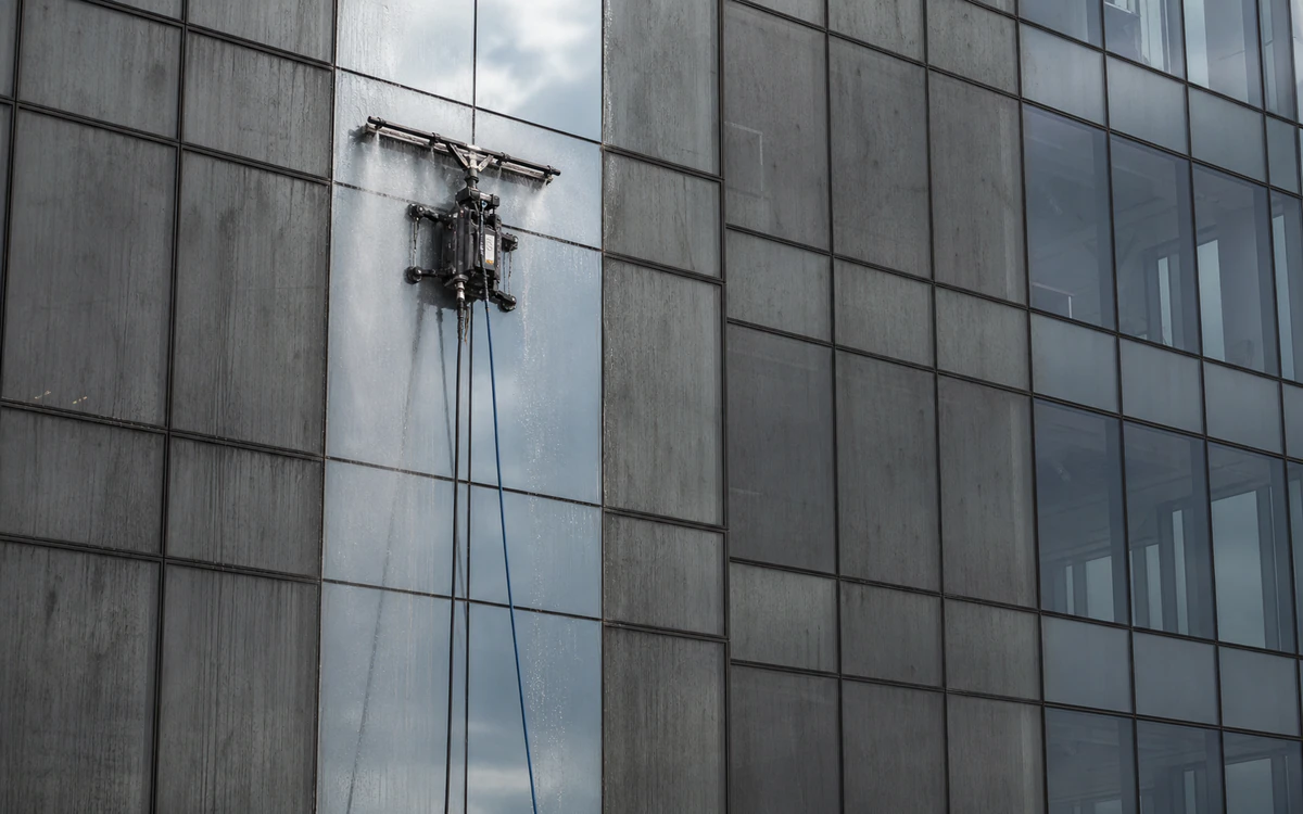 Tethered cleaning drone washing an inaccessible commercial glass facade with a connected low-pressure spray bar